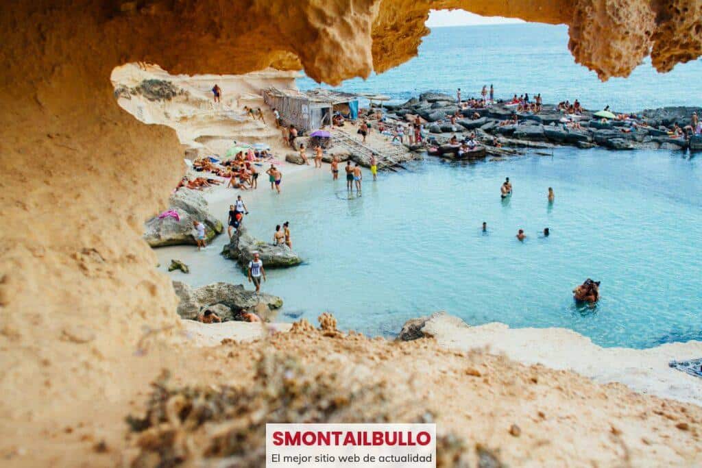 A picturesque beach scene in Spain with people enjoying swimming and sunbathing by rock formations.